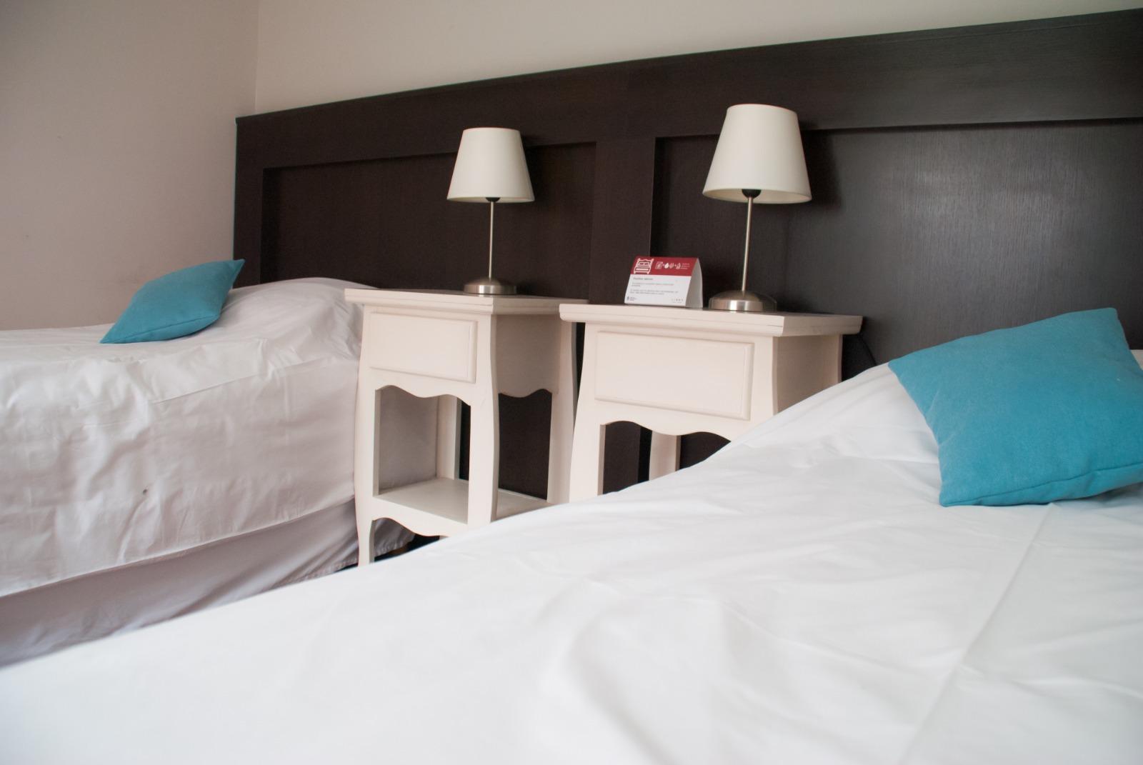 Dormitorio con cama doble, dos mesas de luz y almohadones turquesa