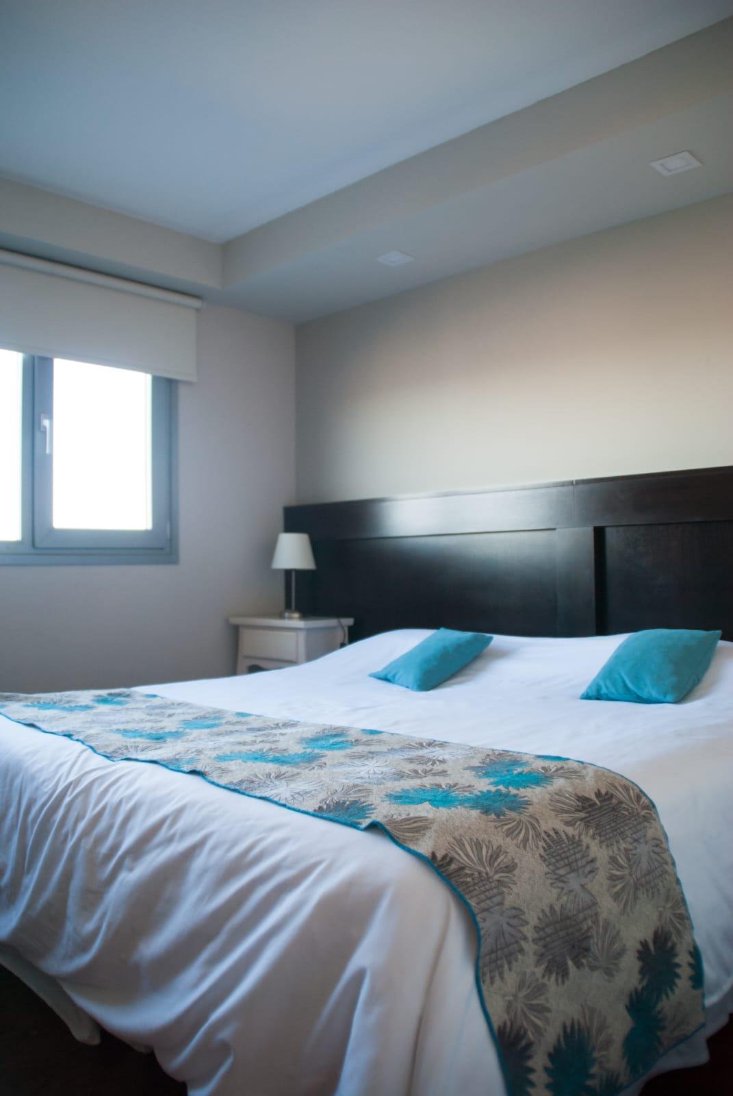 Dormitorio con cama doble y almohadones turquesa