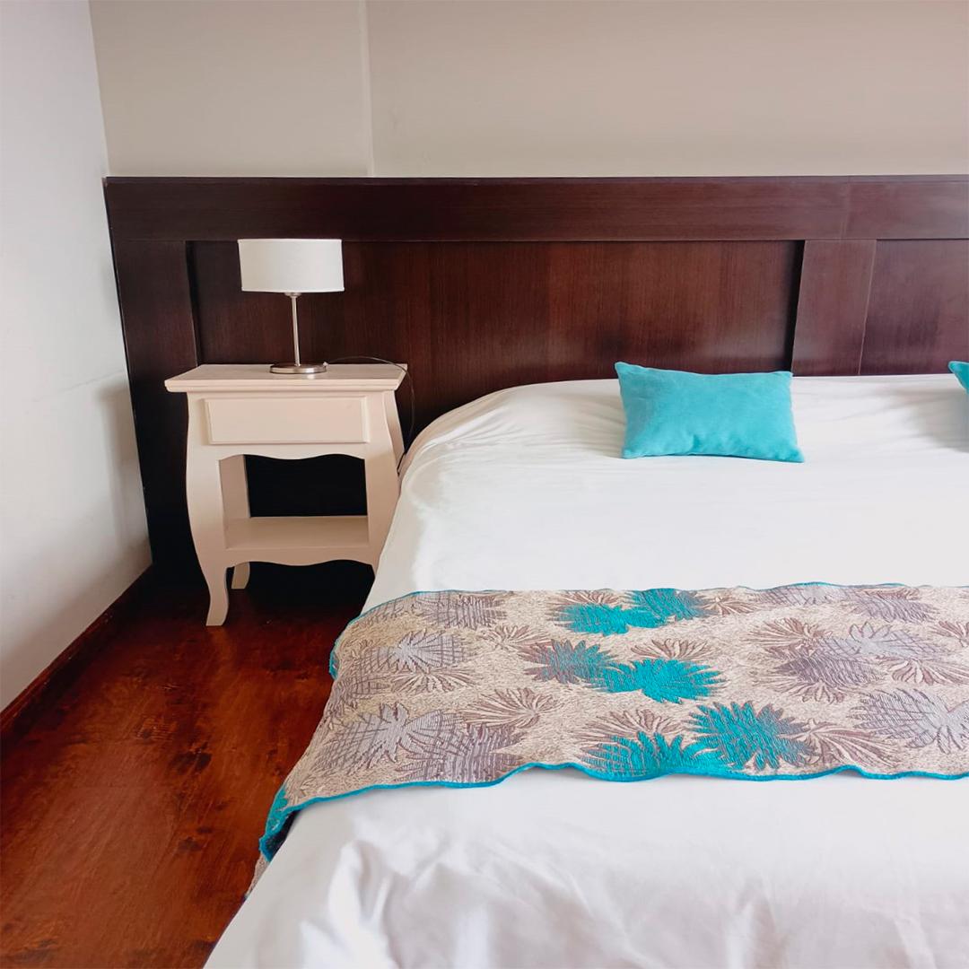 Cama con almohadón turquesa y mesa de luz con lámpara