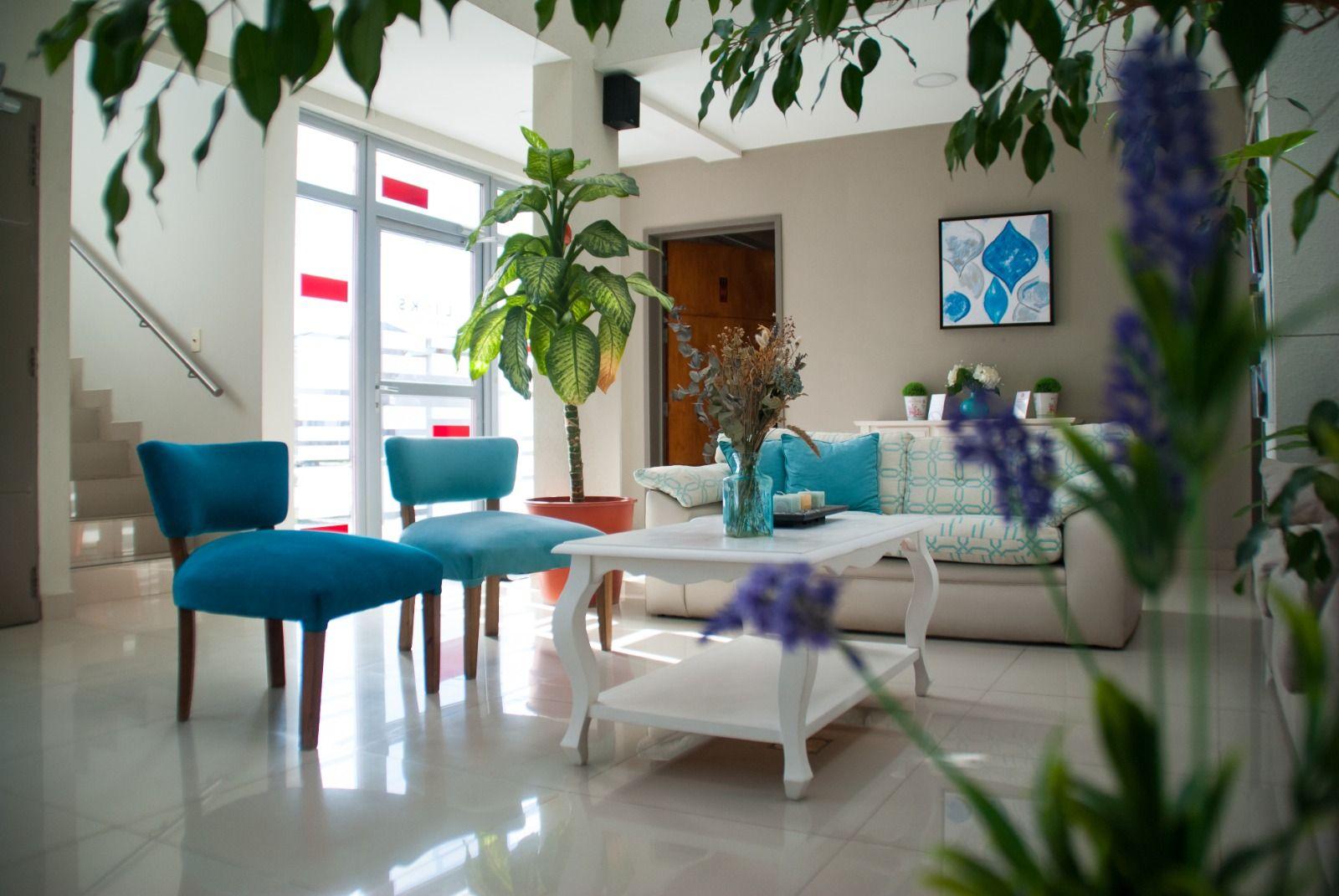 Lobby del hotel con sillas turquesa, plantas y la escalera al fondo